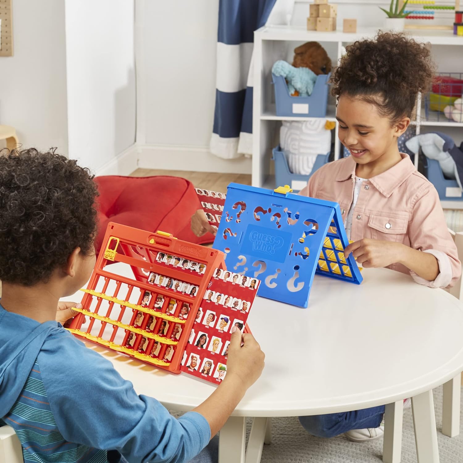 Two children playing Hasbro Guess Who? at a table in a classroom setting.