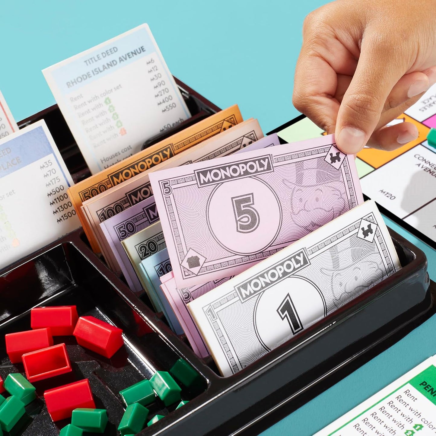 Hand holding Monopoly money with game pieces and cards on a blue background