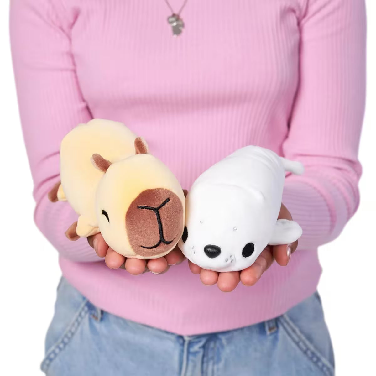 Person holding two small plush toys against a pink sweater background