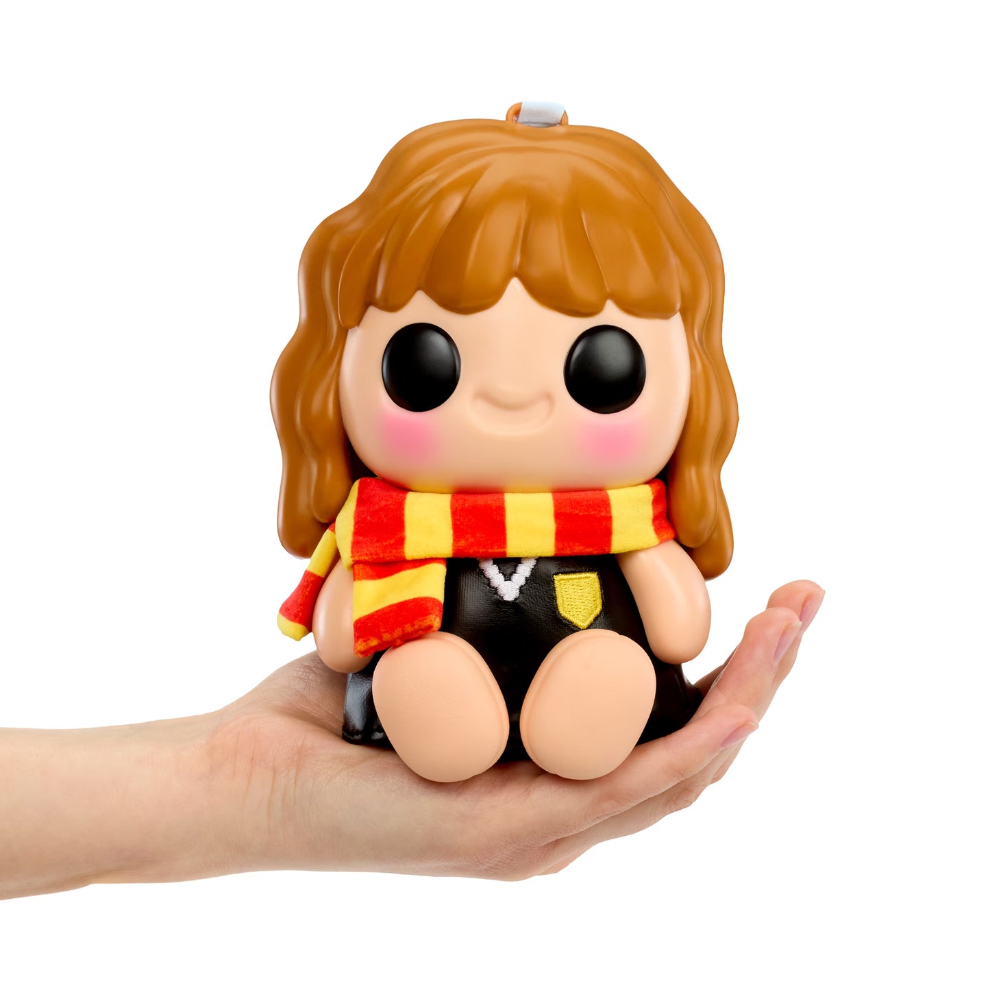 A small stylized doll with brown hair, large black eyes, pink cheeks, and a red-and-yellow striped scarf is being held in a person's hand against a plain white background.