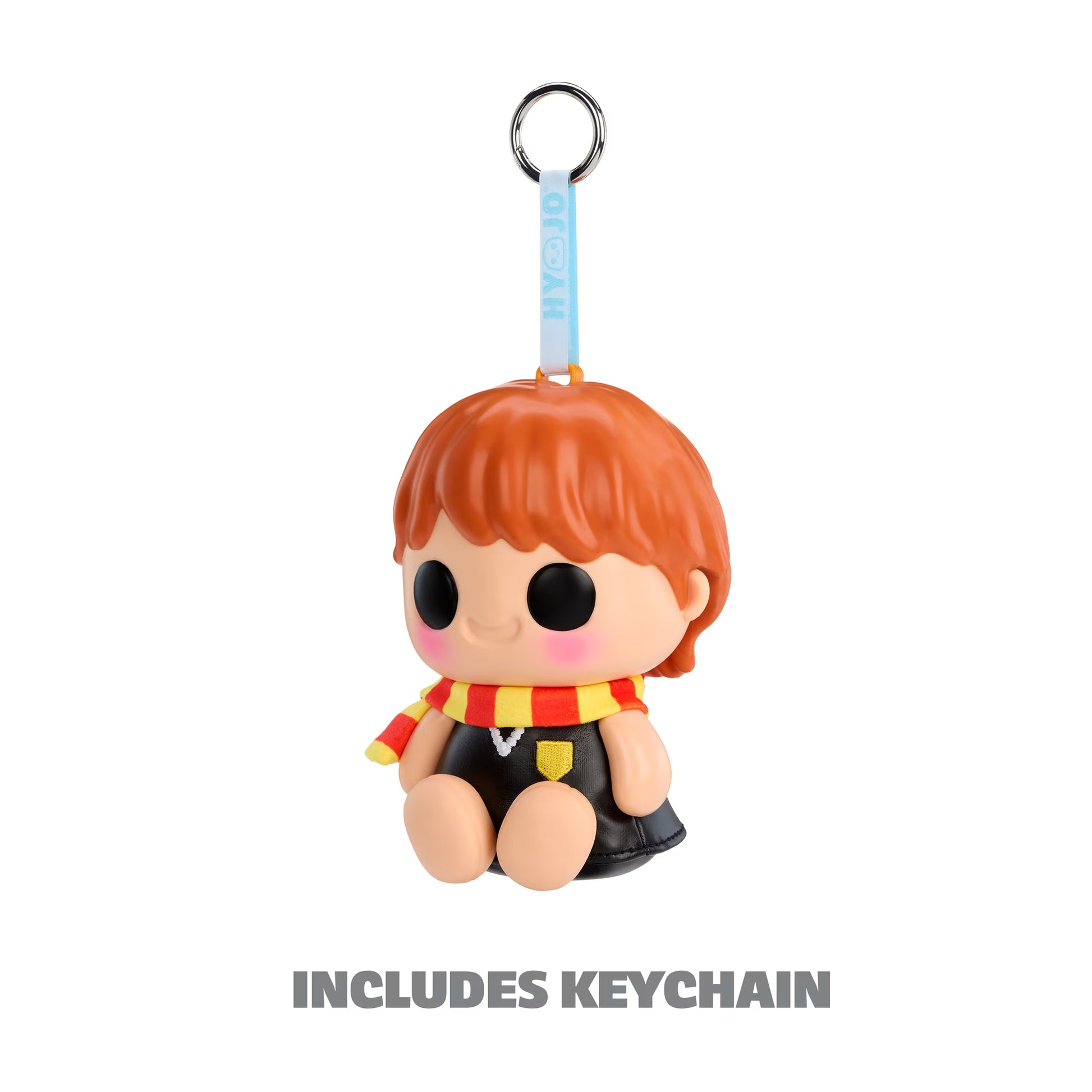 A small character keychain charm with orange hair, a red and yellow striped scarf, and a black outfit, attached to a light blue strap with a metal key ring. The text 'INCLUDES KEYCHAIN' appears below on a white background.