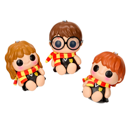 Three small stylized character figurines seated against a plain white background. Each figure has large black eyes, a round head, and a red-and-yellow striped scarf with a small gold crest on a black outfit.