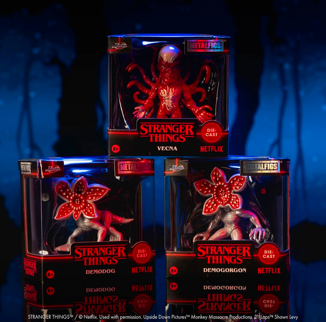 Three Stranger Things die-cast metal figures in retail packaging, arranged against a dark blue forest background. The top figure is Vecna, red, and the bottom two are Demogorgon and Demodog, both with glowing red flower-like heads and pale bodies.