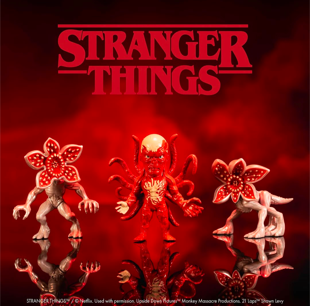 Three Stranger Things collectible figures displayed against a dark red smoky background with the large Stranger Things logo at the top. The center figure is a red multi-armed monster, flanked by two pale flower-headed creatures.