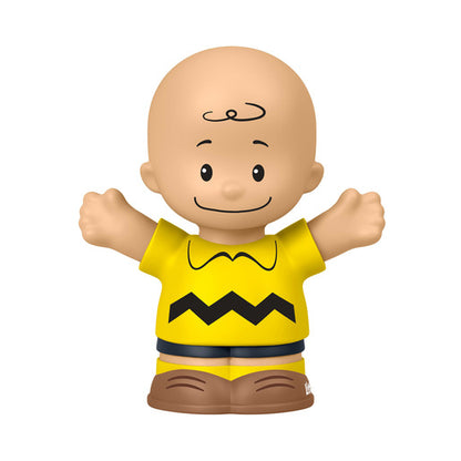A small Charlie Brown toy figure with a bald head, black curly hair detail, and arms outstretched, wearing a yellow shirt with a black zigzag line and brown shorts, isolated on a white background.