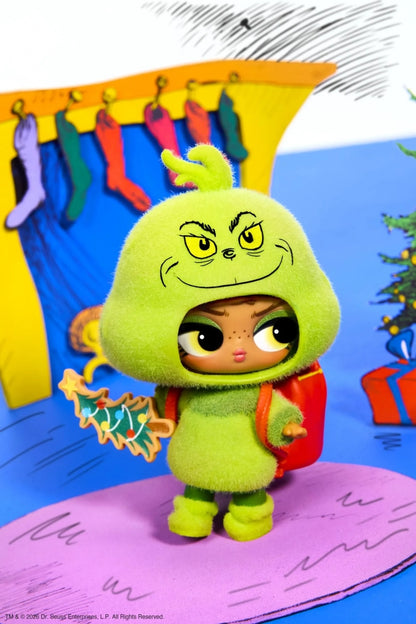 A collectible Grinch-themed action figure wearing a fuzzy lime green hooded outfit with a red backpack, standing on a pink platform against a colorful illustrated backdrop.