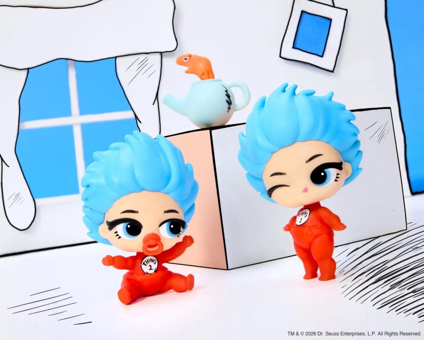 Two small stylized toy figures with bright blue hair and red outfits, posed in front of a hand-drawn white, blue, and peach room scene. One figure is sitting and the other is standing, both wearing a circular emblem on the chest.
