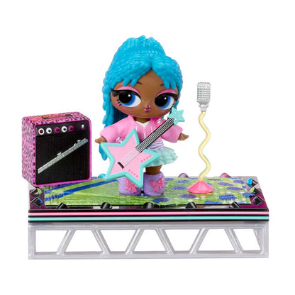 A doll with bright blue hair stands on a small stage holding a pink star-shaped guitar, with a pink-and-black speaker, a silver microphone, and a colorful stage backdrop against a white background.