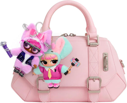 A light pink faux-leather handbag with silver-tone buckles and a top handle, decorated with two LOL Doll plush keychains featuring pink, mint green, and purple outfits.
