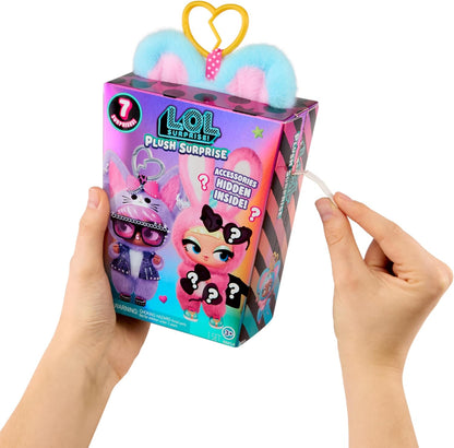 A person's hands holding a LOL Surprise Plush Surprise toy box against a white background. The box features a pink and purple design with cartoon character graphics and a yellow heart-shaped clip on top.