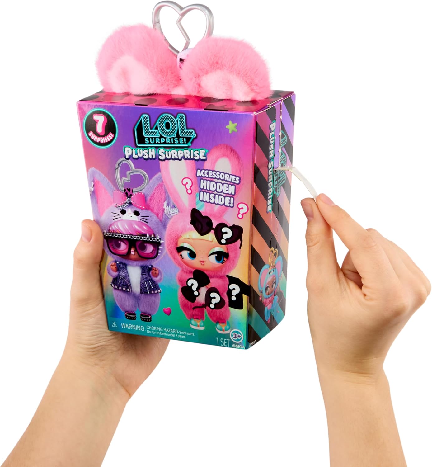 A person holds a colorful LOL Surprise Plush Surprise toy box against a white background. The box features a pink plush character and shows an accessory string being pulled from the side by a hand.