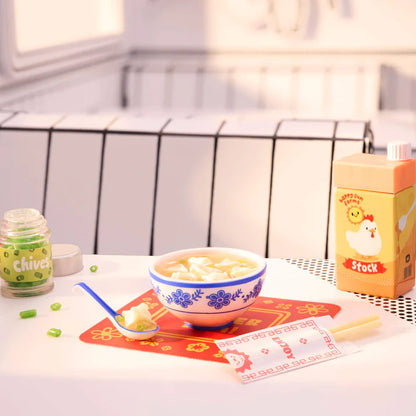 Bowl of soup with a spoon on a table next to a container labeled 'Chives' and a box labeled 'Stock'.
