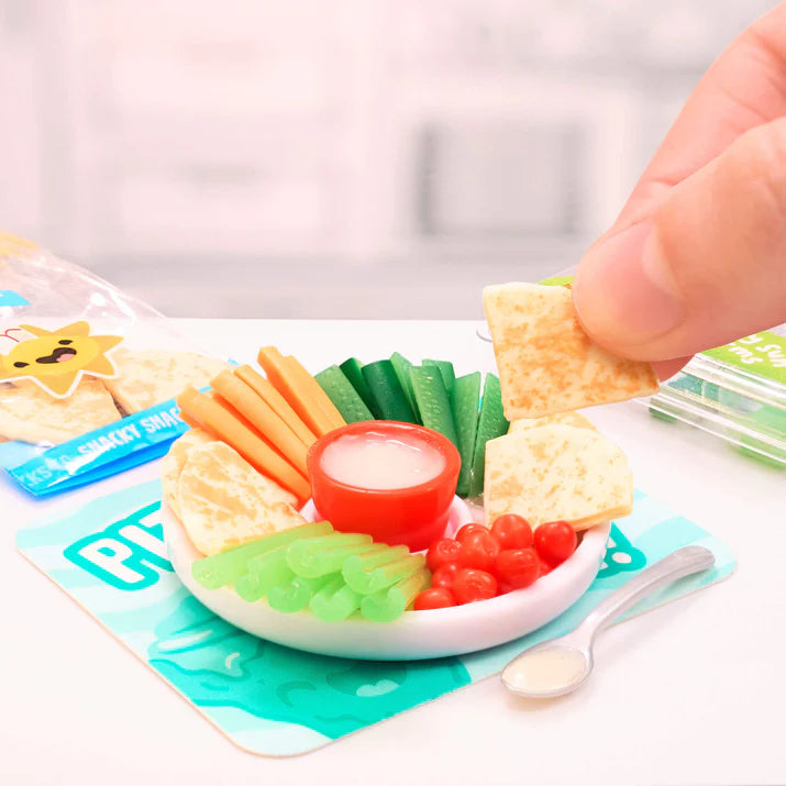 Miniature food set with crackers, vegetables, and dip on a small plate with a hand reaching in.