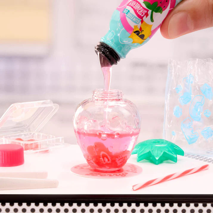 Pink liquid being poured from a bottle into a glass container with colorful ice cubes.