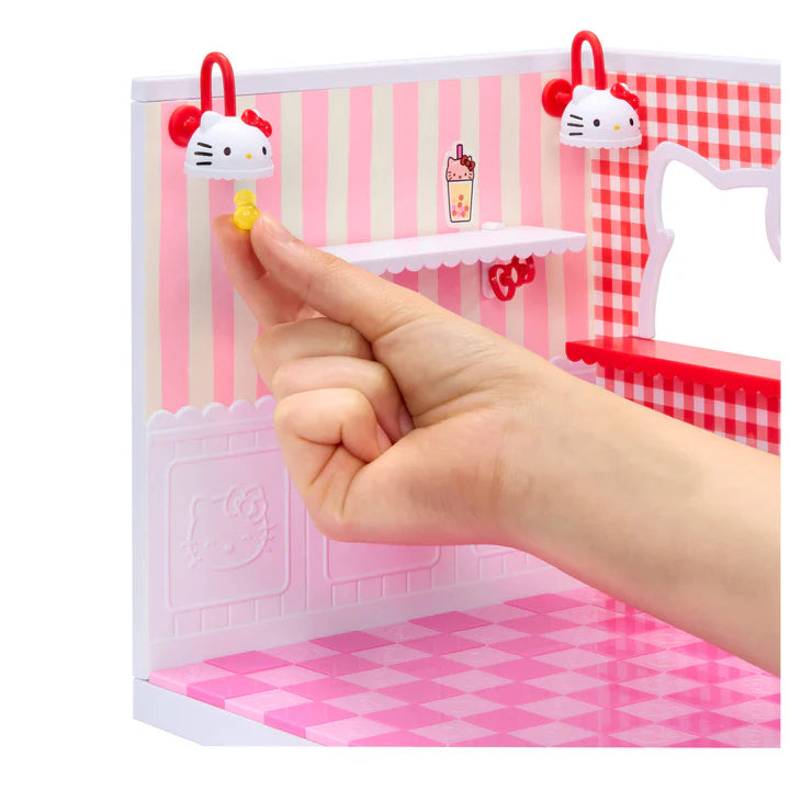 Small model of a kitchen with checkered floor and striped walls, held by a hand from MGA Miniverse Make It Mini Spaces Hello Kitty miniature playset with pink panels and accessories