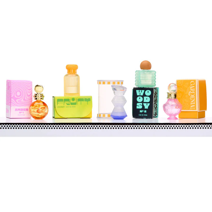 A row of five distinct miniature perfume bottles lined up on a white surface, featuring various shapes and colors including Amber, Fruity Coconut, and Woody scents.