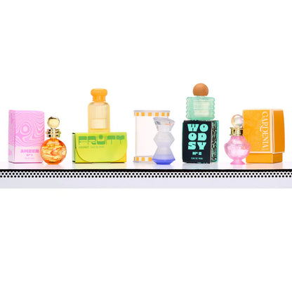 A row of five distinct miniature perfume bottles lined up on a white surface, featuring various shapes and colors including Amber, Fruity Coconut, and Woody scents.