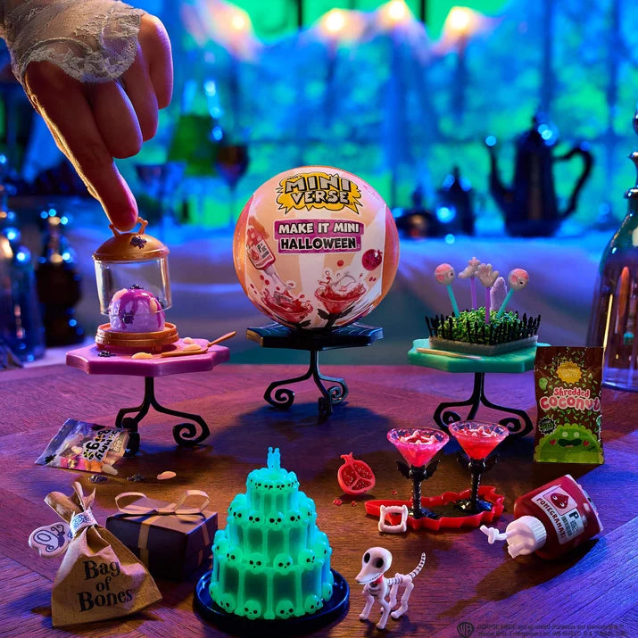 A tabletop display of a mini Halloween toy set under colorful neon lighting. A hand is visible at the top left touching one of the small accessories.