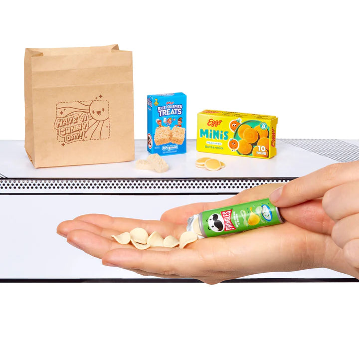 A hand pouring miniature potato chips out of a tiny Pringles Sour Cream & Onion can, sitting next to boxes of Kellogg's Rice Krispies Treats and Eggo Minis.