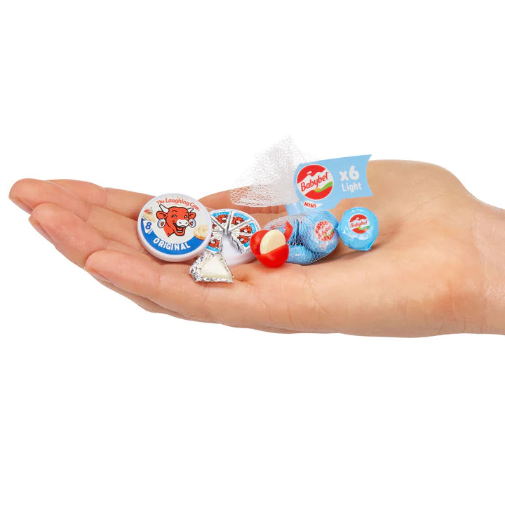 A hand holding miniature cheese replicas, including a Laughing Cow wheel with wedges and a mesh bag of Mini Babybel Light cheese.