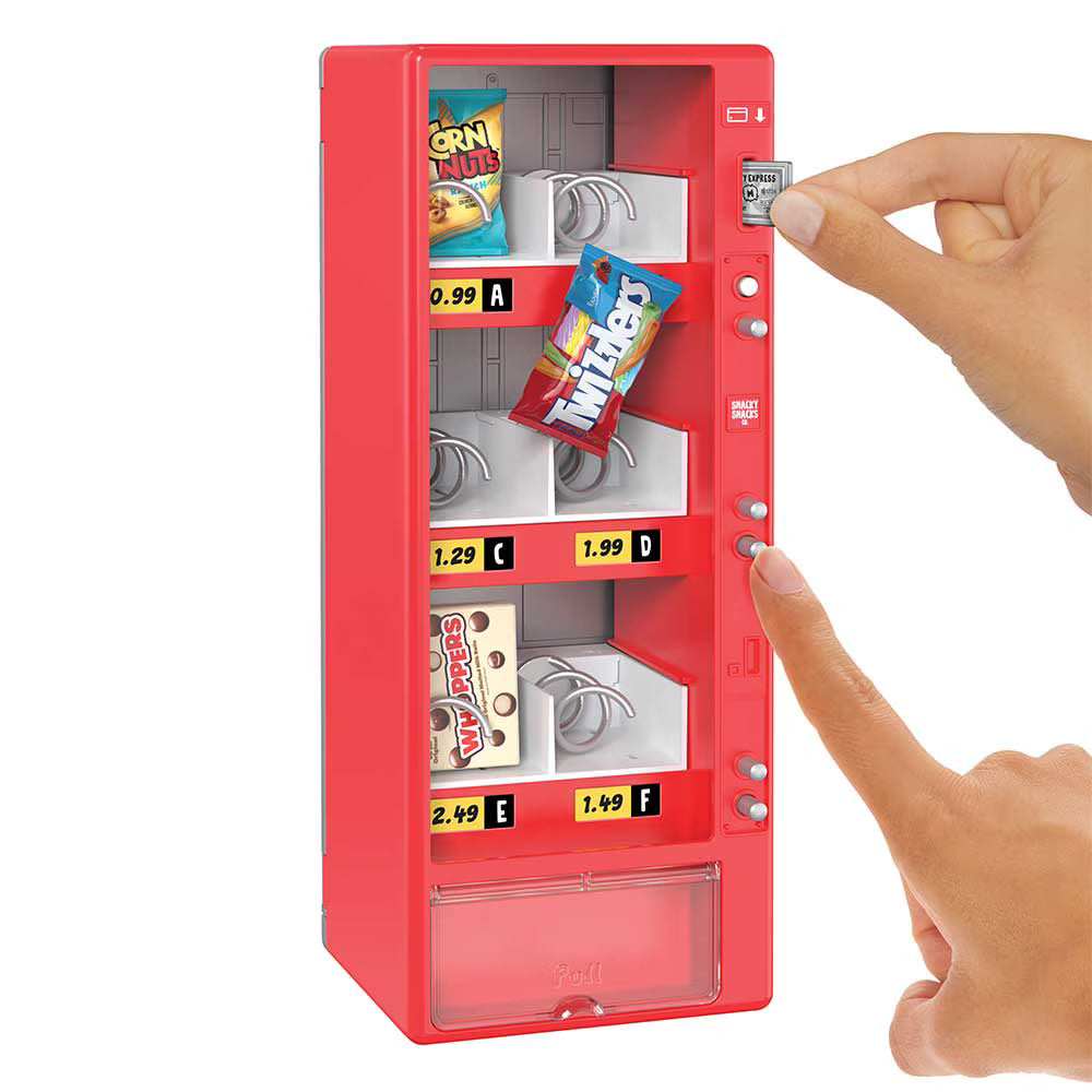 A miniature red toy vending machine with compartments and buttons, shown on a white background with a person's hand pressing a button and another hand holding a small KitKat packet.
