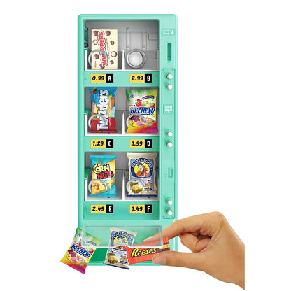A mint green toy vending machine with colorful snack displays, shown on a white background with a hand reaching in to pull out candy bags and a Reese's bar.