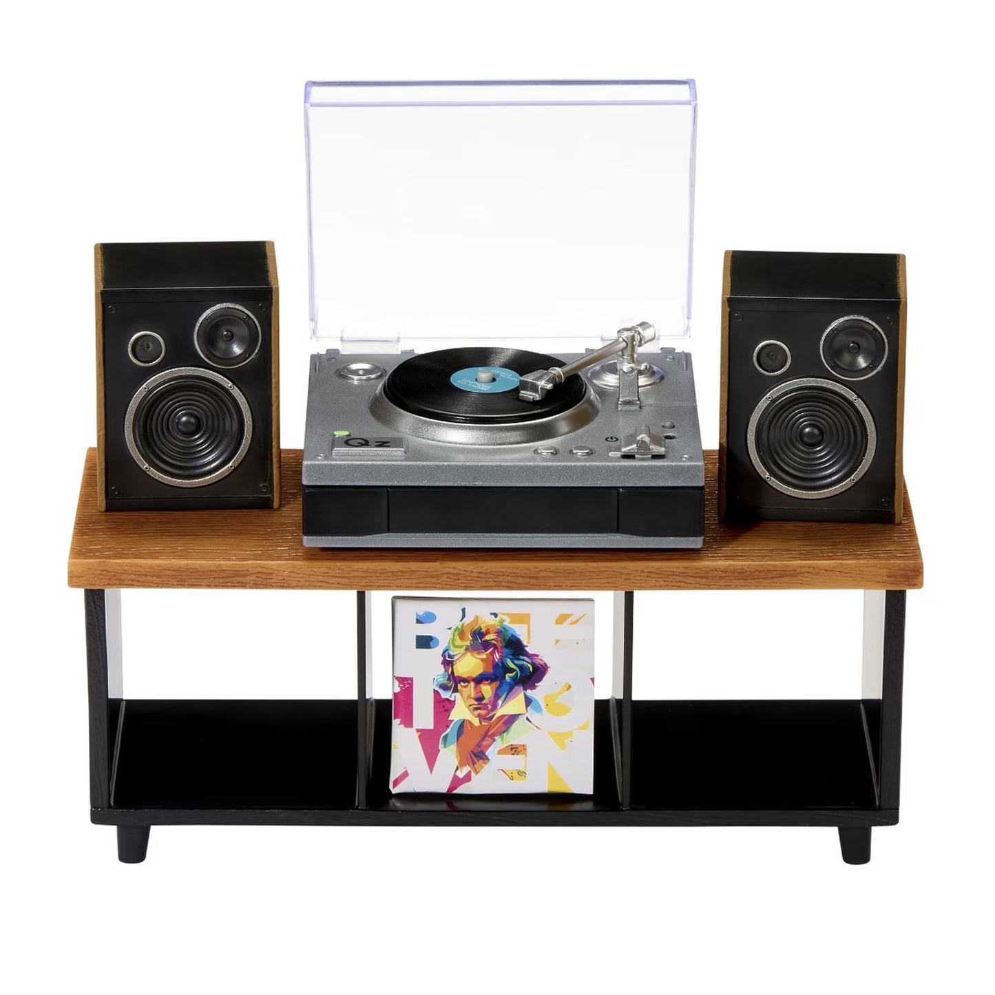 A retro-style record player console with a wooden top shelf, black metal legs, two black speakers, a silver and black turntable with a clear dust cover open, and a vinyl record on the platter. A framed colorful art print hangs below on a white background.