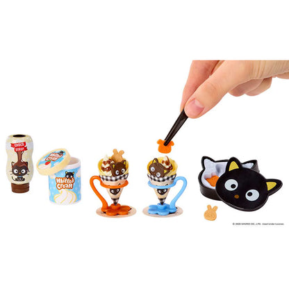 A miniature toy set featuring small character figures and accessories on a white background, with a human hand holding a black tool above one of the figures. The set includes a small brown bottle figure, a blue ice cream container figure, two dessert cone figures in orange and blue, and a black cat-shaped bowl or container with a small beige accessory.