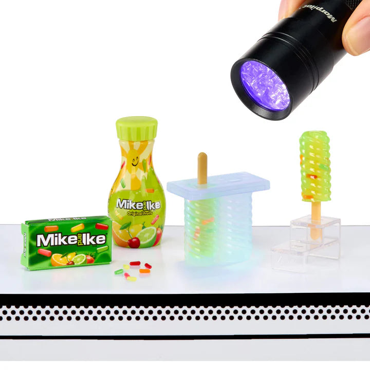 A Mike and Ike themed Miniverse set showing a green resin bottle, a box of candy, and a popsicle mold being cured under a UV flashlight beam.