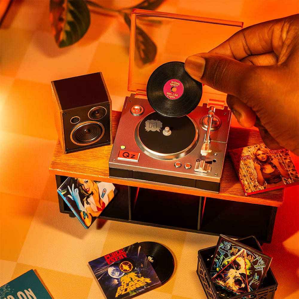 A hot pink mystery blind pack ball for MGA's Miniverse Real Music Vinyl surrounded by mini playable vinyl records, sleeves, and crates.