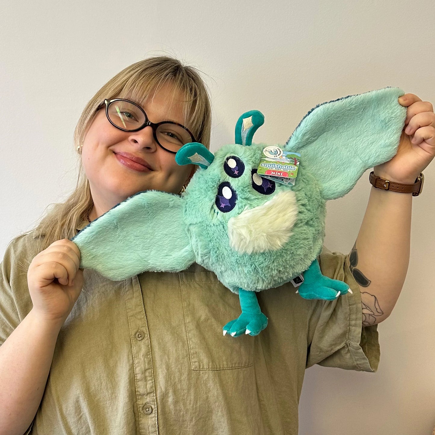 Person holding a green plush toy with a plain background