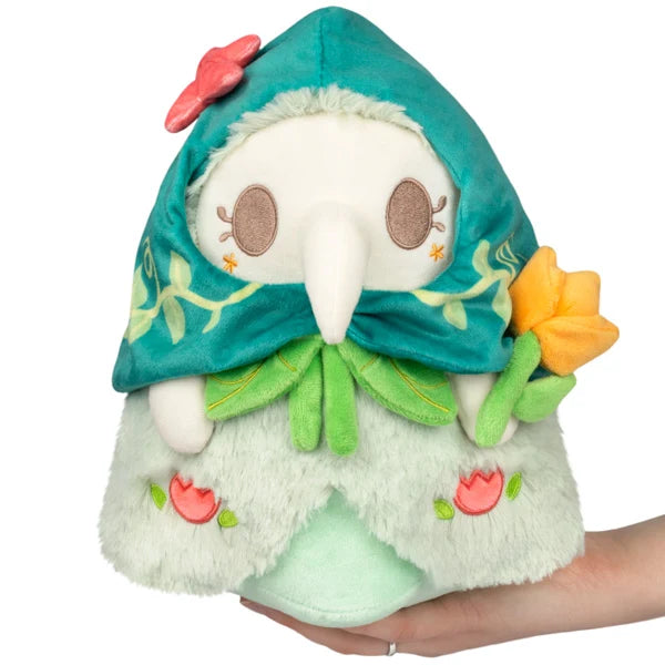Mini Squishable Botanical Plague Nurse plush with teal vine-embroidered hood, white beak, light green dress, and holding an orange flower.