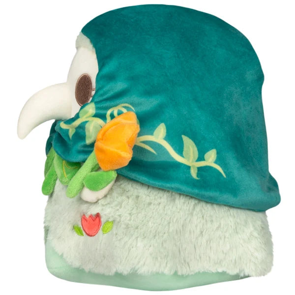 Mini Squishable Botanical Plague Nurse plush with teal vine-embroidered hood, white beak, light green dress, and holding an orange flower.