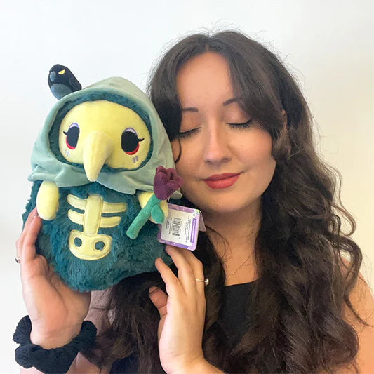 Woman holding Mini Squishable Graveyard Plague Nurse plush with green cloak, skeleton embroidery, rose, and bat