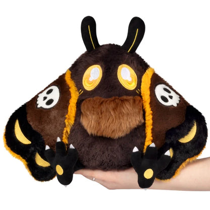 Mini Squishable Hawkmothman plush featuring dark brown fur, yellow eyes, and dark wings with skull patterns.
