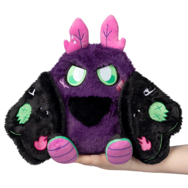 Mini Squishable Neon Punk Mothman plush with deep purple fur, neon pink antennae, bright green eyes, and patch-embellished black wings.