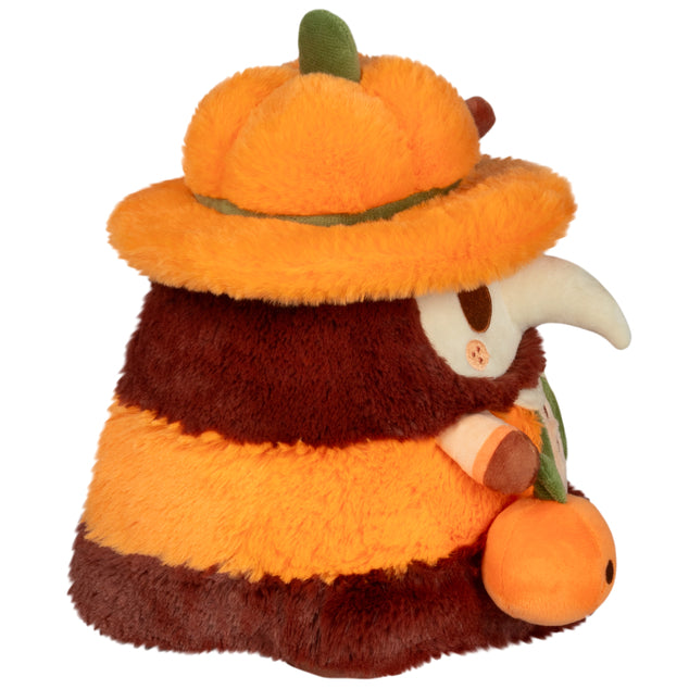 Side view of Mini Squishable Pumpkin Spice Doctor Plague plush with pumpkin hat and cinnamon stick