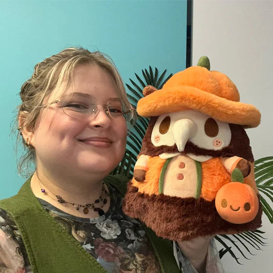 Woman holding Mini Squishable Pumpkin Spice Doctor Plague plush with pumpkin hat and cinnamon stick