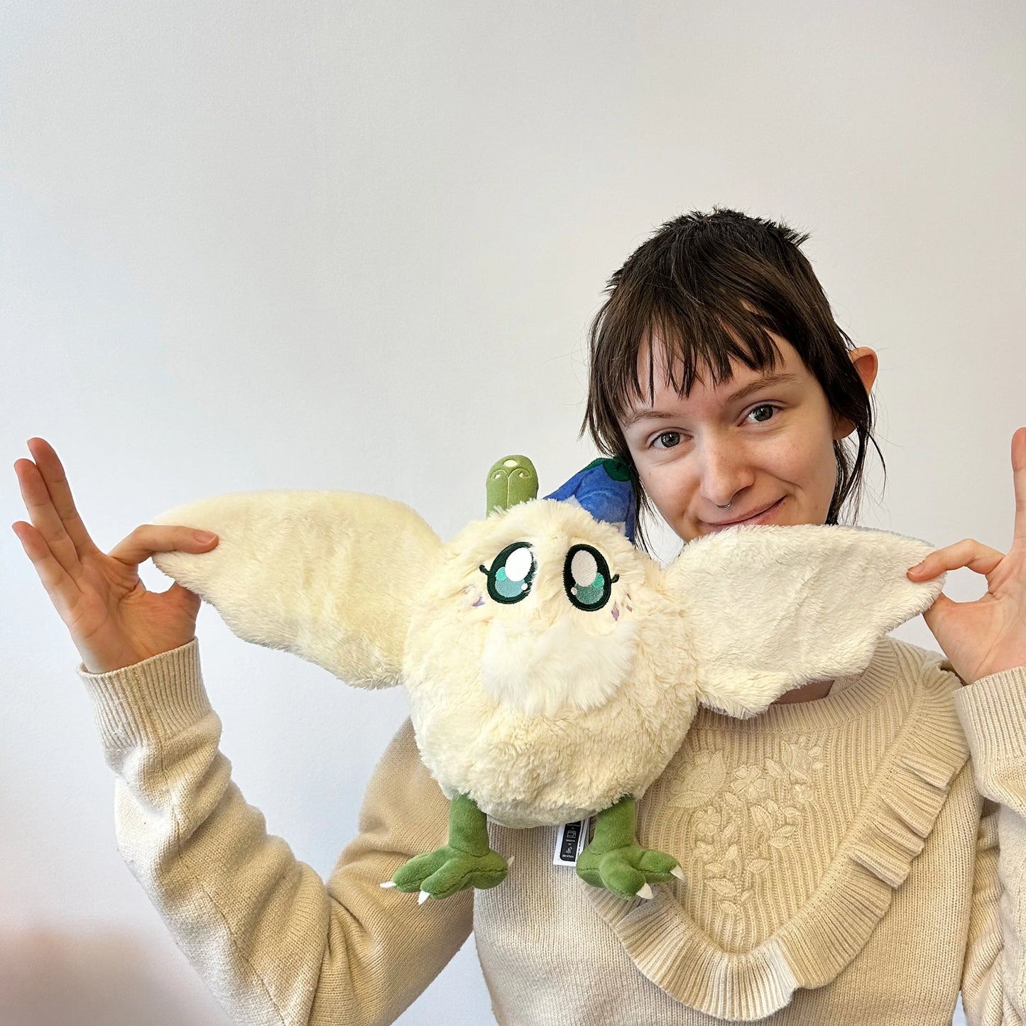 Person holding a plush toy resembling a creature with large eyes and wings.