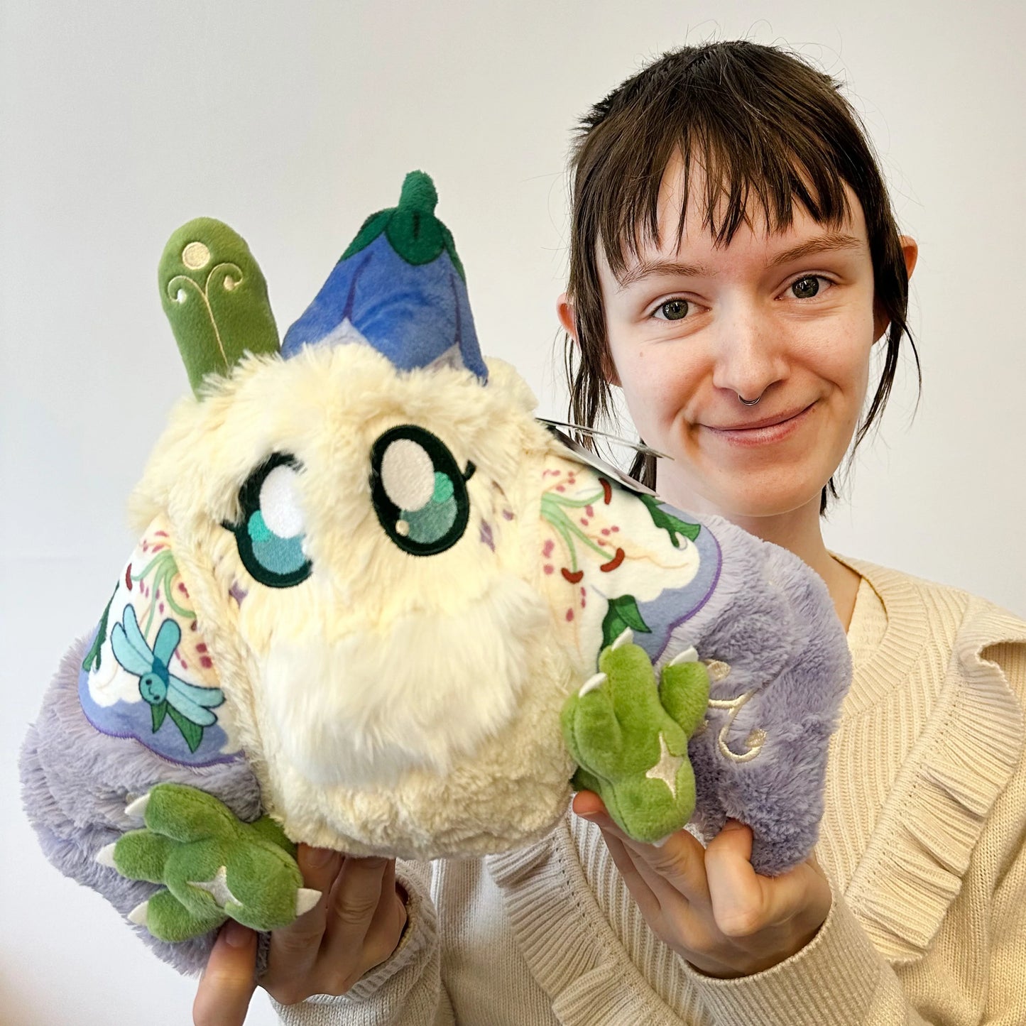 Person holding a plush toy with a white face and colorful accents