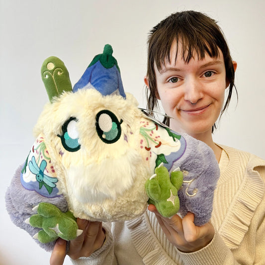Person holding a plush toy with a white face and colorful accents