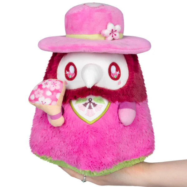 Squishable Mini Sakura Plague Doctor 10-Inch Plush, a vibrant pink and magenta soft toy with a floral fan and cherry blossom accents