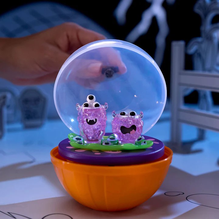 Toy with purple characters inside a transparent ball on an orange base, held by a hand.  Miniverse Make it Mini Halloween Series 3.