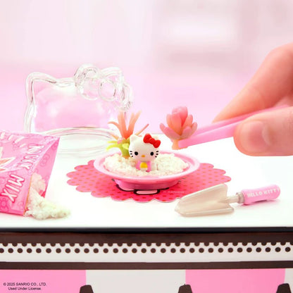 Hello Kitty-themed playset with a hand interacting with it on a pink and white background. Miniverse Make It Mini Hello Kitty Series 2.