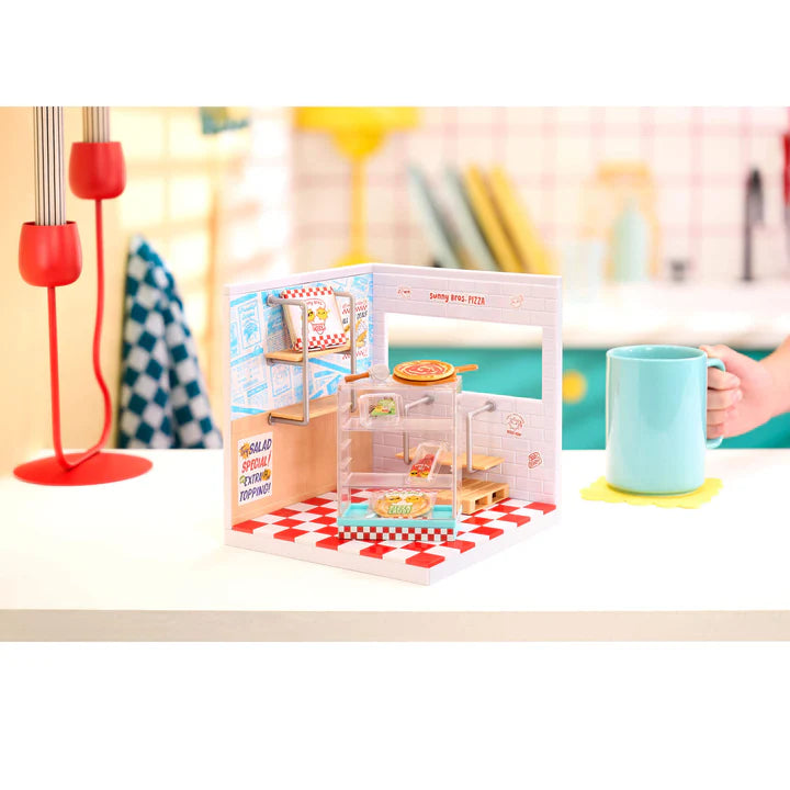Toy kitchen set from Miniverse Spaces Pizza Shop Starter Pack display set Canada on a table with a mug and lamp in the background