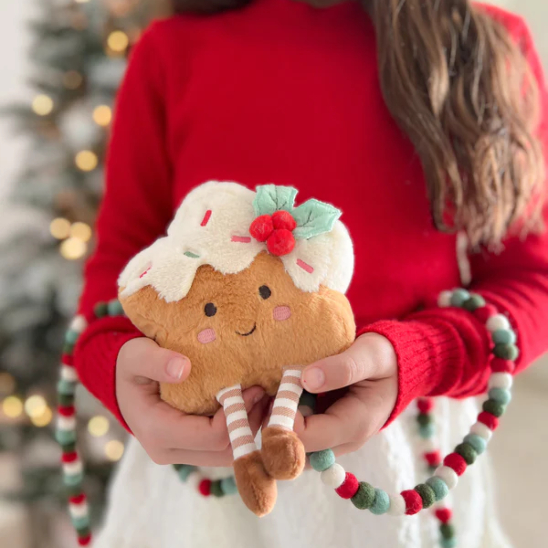 Person holding a plush gingerbread man toy with a Christmas tree in the background
