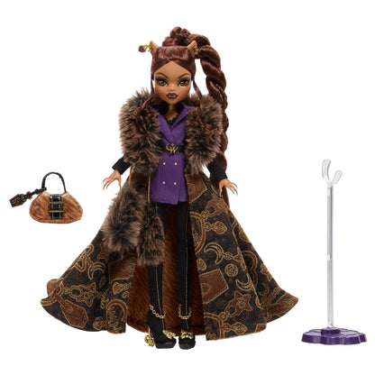Doll with long brown hair styled in pigtails, wearing a purple outfit with a fur-lined coat, standing next to a handbag and a stand on a white background.