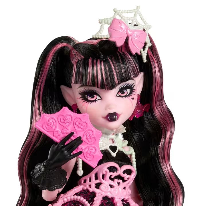 Monster High doll with black and pink hair, wearing a tiara and holding pink fans on a white background