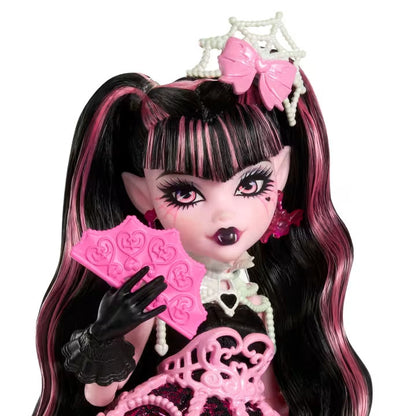 Monster High doll with black and pink hair, wearing a tiara and holding pink fans on a white background