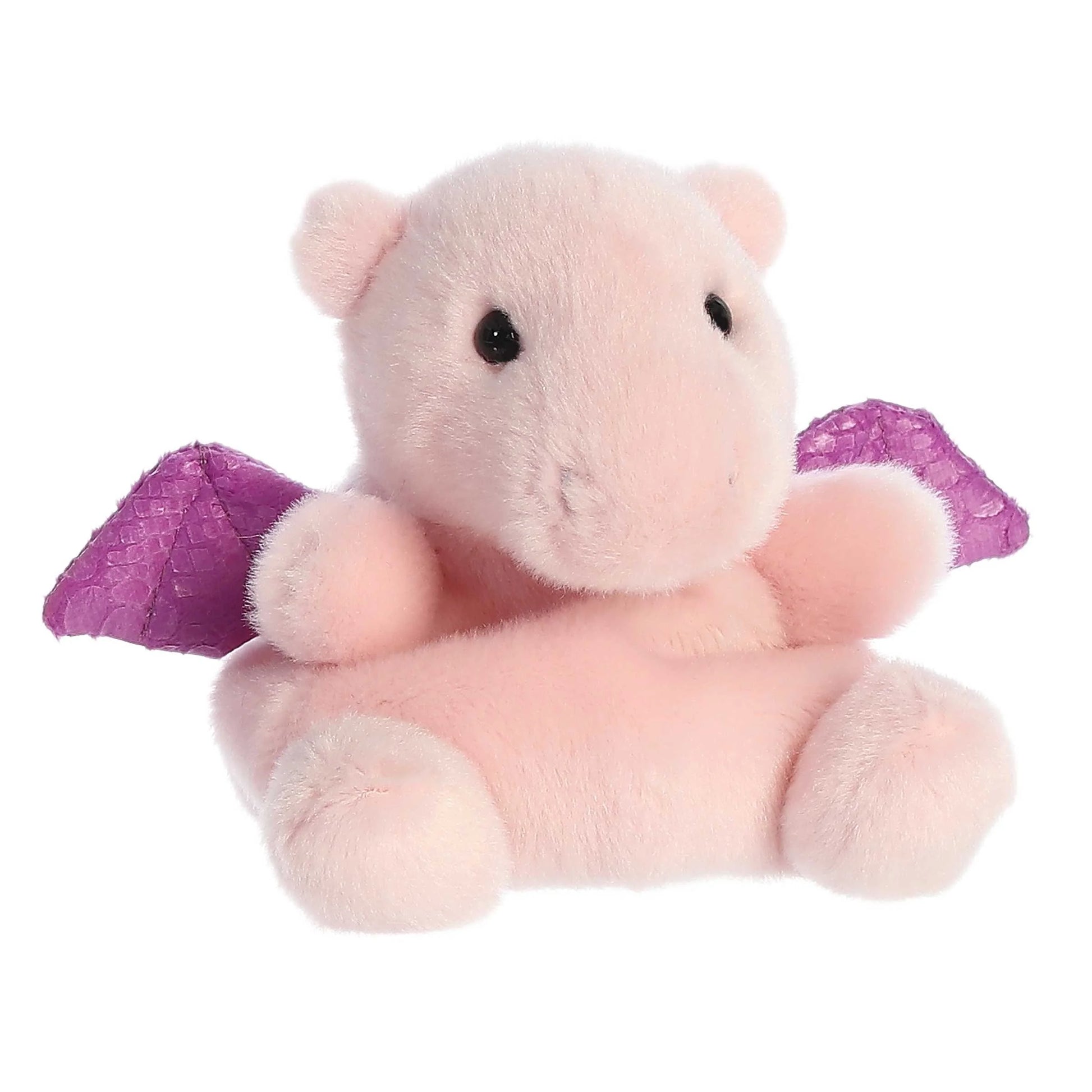 A small, soft pink plush dragon (Palm Pals Aria) sitting down, with shiny, textured purple wings and small black eyes.